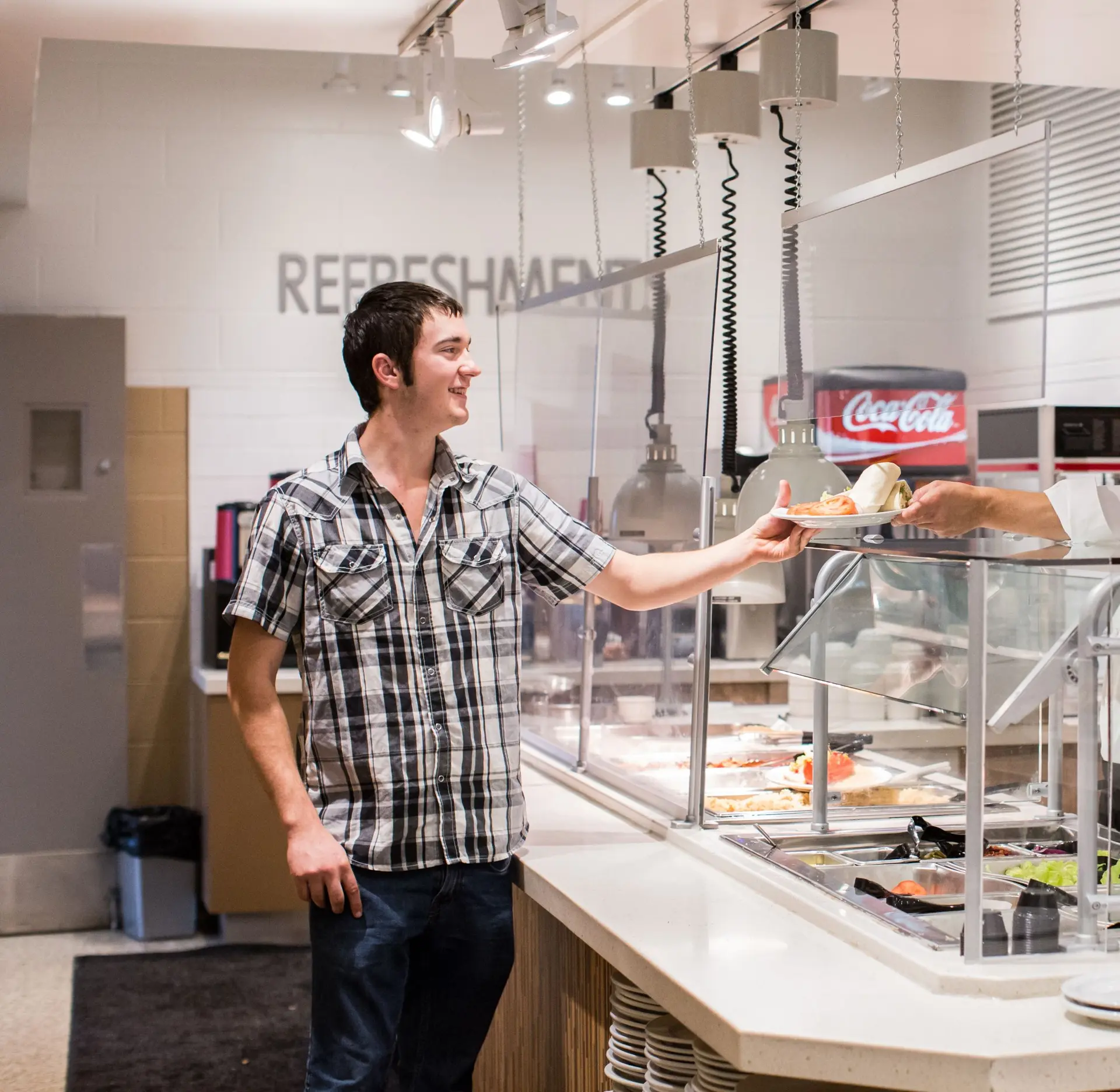 Photo of student receiving food in cafeteria on a plate.
