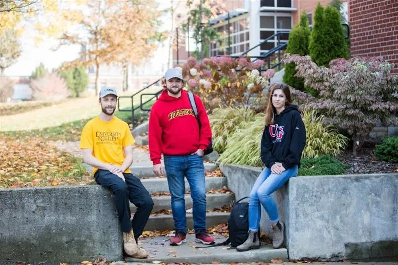 Three students sitting at stairs infront of campus building.