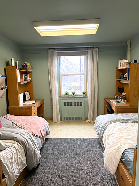 Image of two single beds in green painted room with window at center and two wooden desks on either side