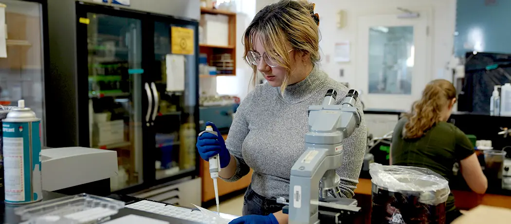 Photo of female in lab looking at microscope.